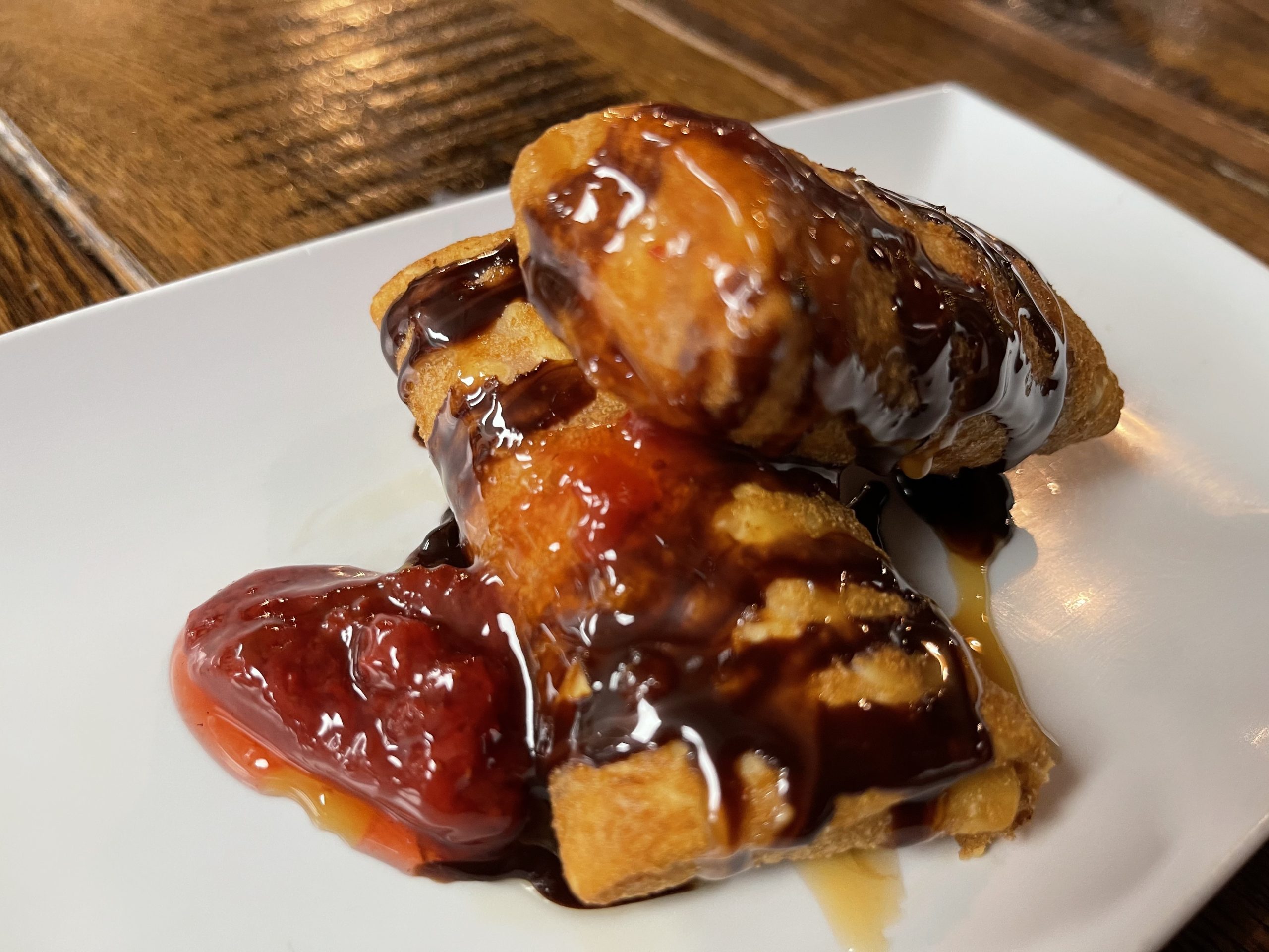 Decadent Raspberry Chimi from Atwater Street Tacos, combining raspberries and cream cheese in a fried tortilla, drizzled with chocolate syrup and caramel, garnished with fresh strawberries, presenting a fusion of classic Mexican flavors with a sweet twist.